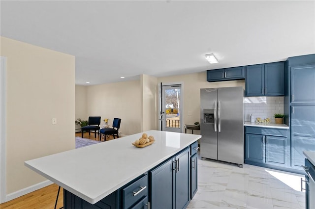 kitchen with a center island, marble finish floor, light countertops, decorative backsplash, and stainless steel fridge