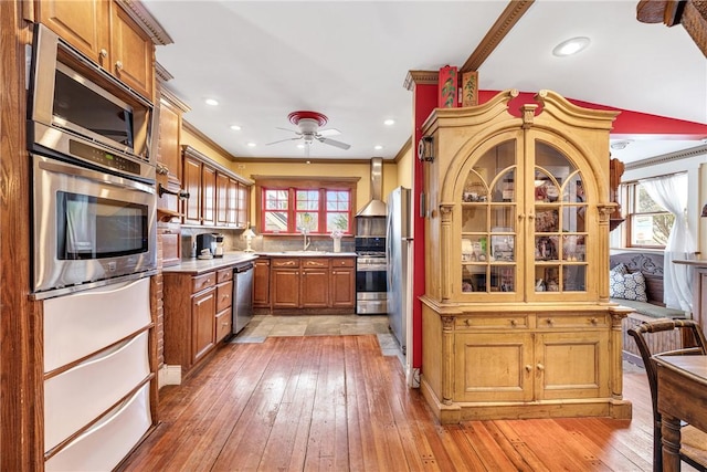 kitchen with a sink, light countertops, ornamental molding, appliances with stainless steel finishes, and light wood-type flooring