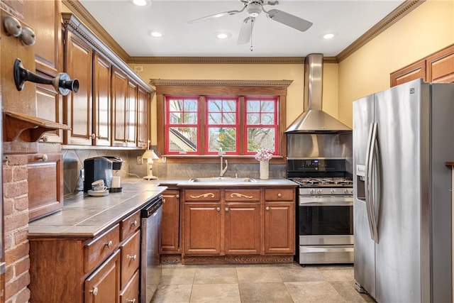 kitchen with tile countertops, wall chimney exhaust hood, appliances with stainless steel finishes, brown cabinets, and a sink