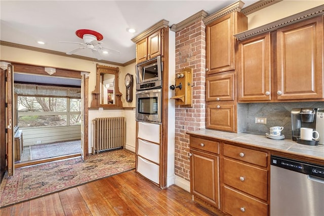 kitchen featuring tile countertops, stainless steel appliances, ornamental molding, backsplash, and radiator heating unit