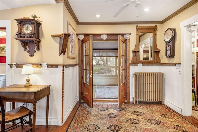 foyer entrance featuring wainscoting, crown molding, radiator heating unit, and wood finished floors