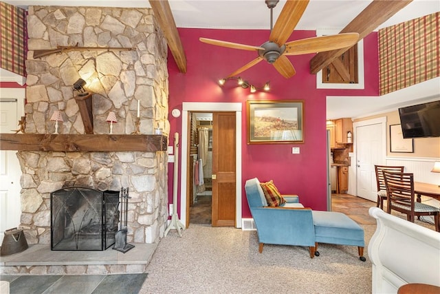 carpeted living area featuring ceiling fan, visible vents, beam ceiling, and a stone fireplace