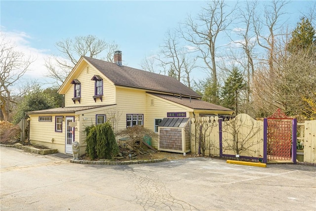 view of property exterior featuring uncovered parking, a gate, fence, and a chimney