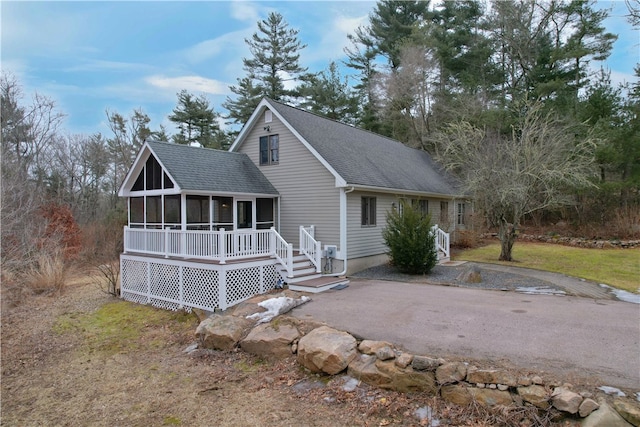 view of front of home with a sunroom, roof with shingles, and driveway