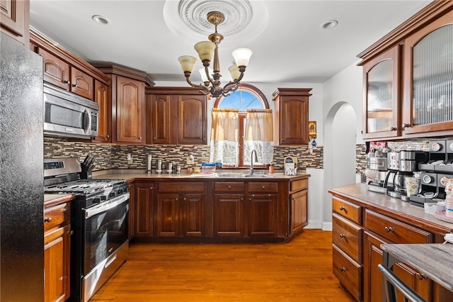 kitchen with arched walkways, wood finished floors, a sink, appliances with stainless steel finishes, and backsplash