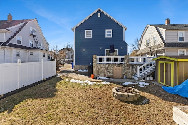 back of property with a deck, an outdoor fire pit, an outdoor structure, fence, and stairs