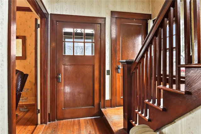 foyer entrance with stairs, wood finished floors, and wallpapered walls