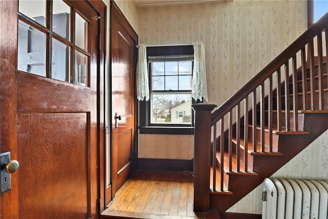 interior space with wallpapered walls, radiator heating unit, baseboards, and hardwood / wood-style floors