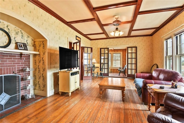 living area featuring wallpapered walls, coffered ceiling, hardwood / wood-style flooring, ornamental molding, and a brick fireplace