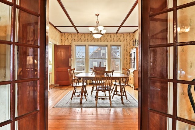 dining room featuring a notable chandelier, light wood-style floors, coffered ceiling, and wallpapered walls