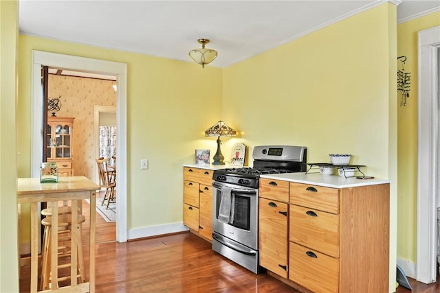 kitchen featuring dark wood-style flooring, baseboards, light countertops, stainless steel gas range, and crown molding