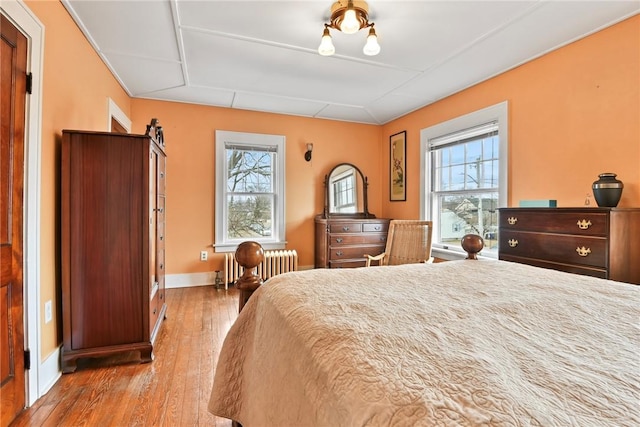 bedroom featuring baseboards, multiple windows, radiator heating unit, and wood finished floors