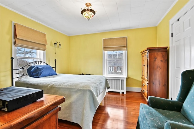 bedroom featuring radiator heating unit, crown molding, baseboards, and wood finished floors