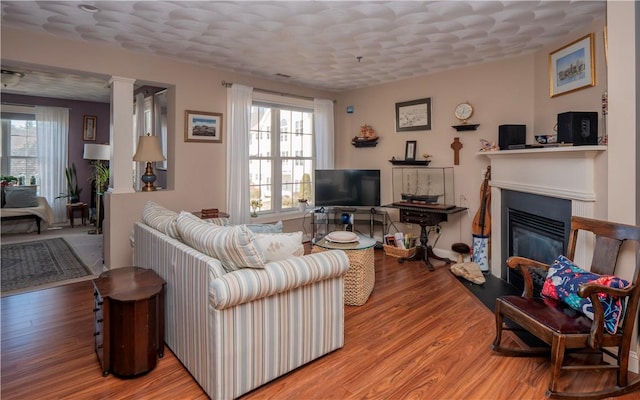 living area with a glass covered fireplace, wood finished floors, and decorative columns