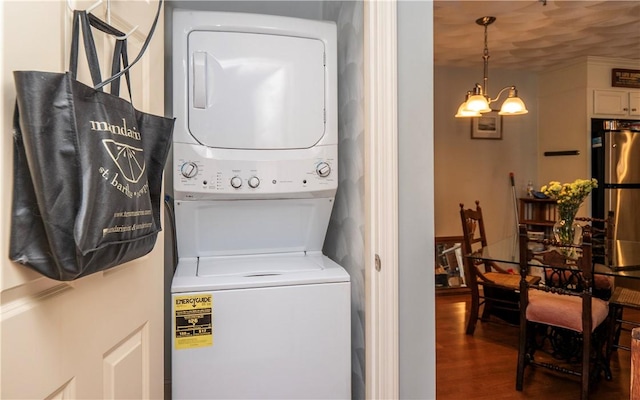 laundry area featuring wood finished floors, stacked washer and clothes dryer, an inviting chandelier, and laundry area