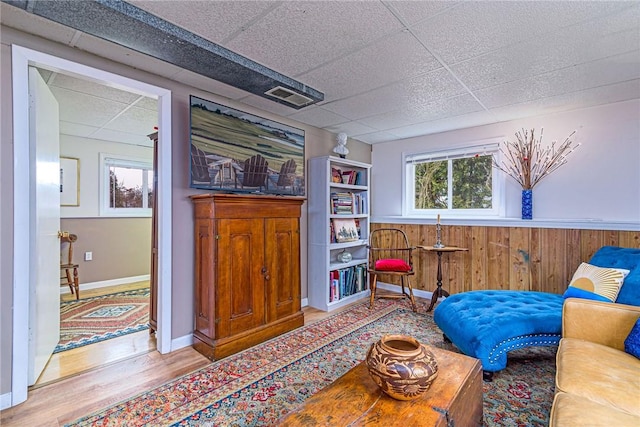 sitting room with wood walls, a drop ceiling, a wealth of natural light, and wood finished floors