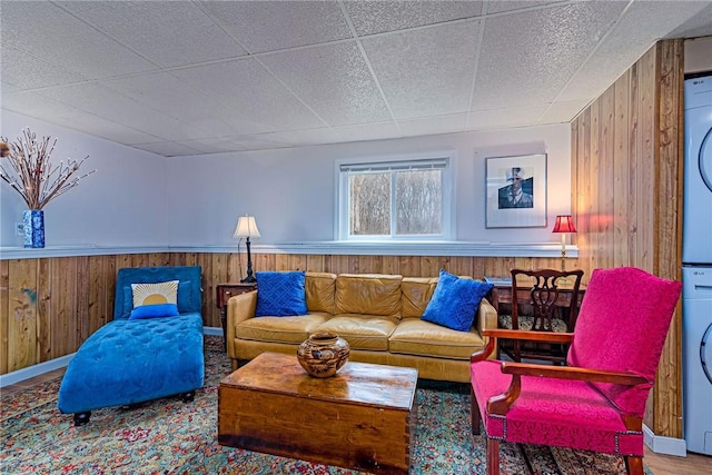 living area featuring stacked washer and dryer, wooden walls, and wainscoting