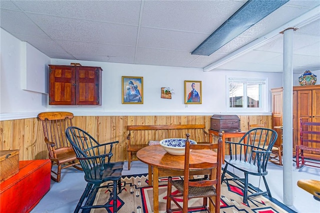 dining area featuring finished concrete flooring, a wainscoted wall, wooden walls, and a drop ceiling