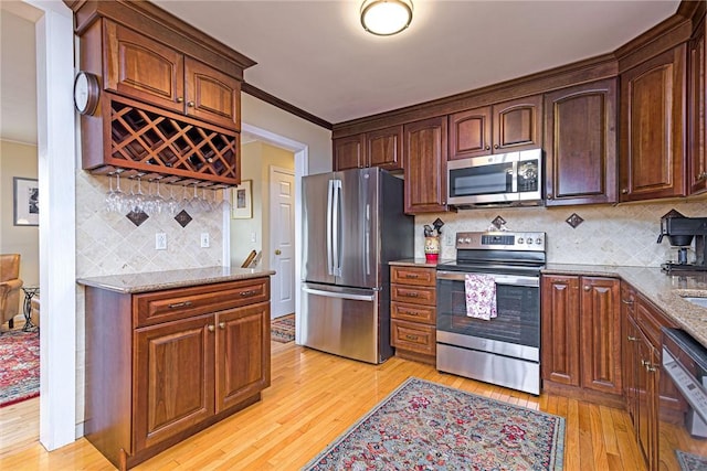 kitchen with light stone counters, crown molding, light wood finished floors, stainless steel appliances, and backsplash