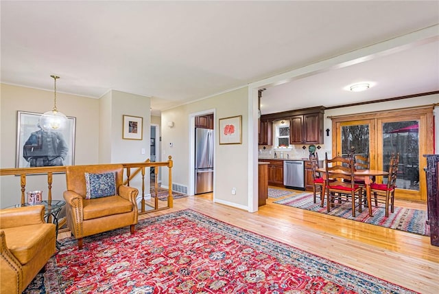 living area with baseboards, light wood-type flooring, visible vents, and crown molding