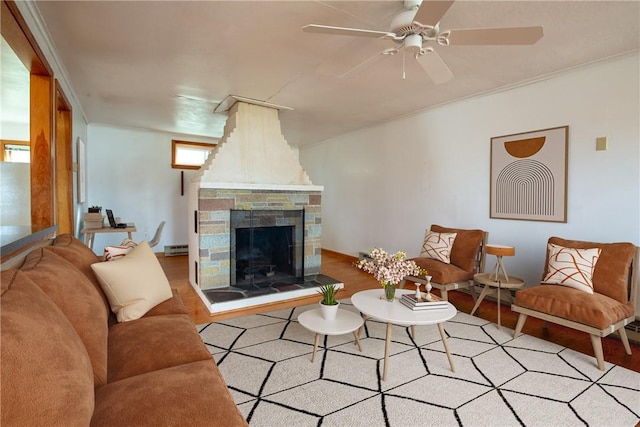 living room with a healthy amount of sunlight, crown molding, ceiling fan, a stone fireplace, and baseboard heating