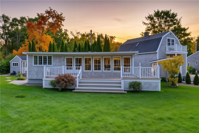 back of property at dusk featuring a gambrel roof, a lawn, and a deck