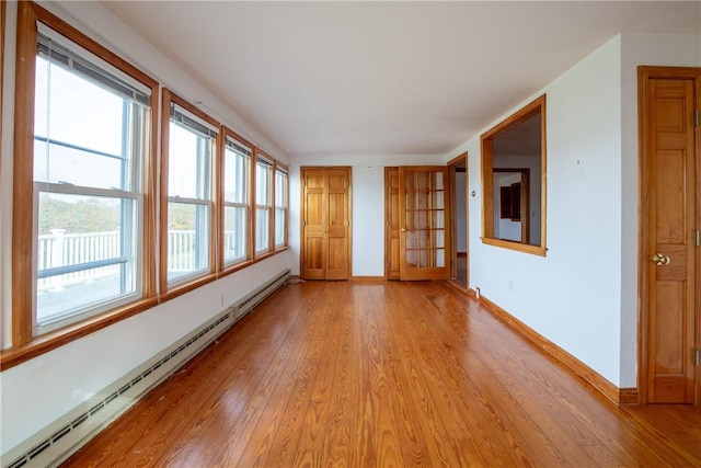 empty room featuring a baseboard heating unit, baseboards, and light wood-style flooring