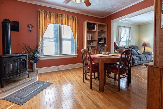 dining area featuring ceiling fan, baseboards, hardwood / wood-style floors, a wood stove, and crown molding