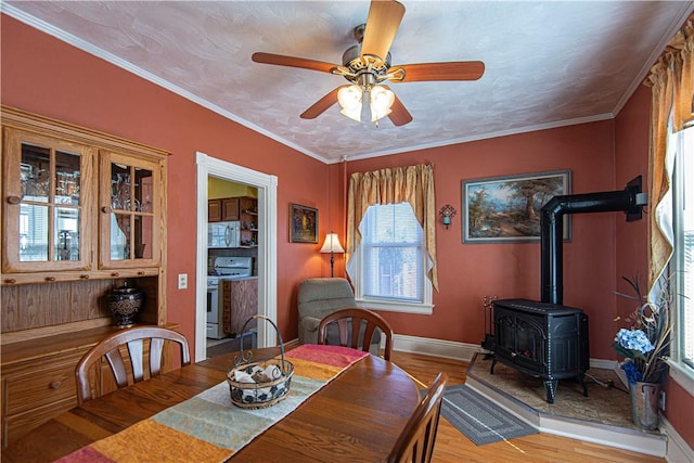 dining space with ornamental molding, a ceiling fan, a wood stove, light wood-type flooring, and baseboards