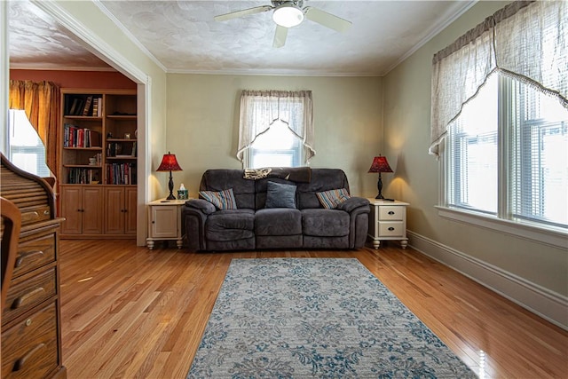 living room with light wood-style floors, ceiling fan, baseboards, and crown molding