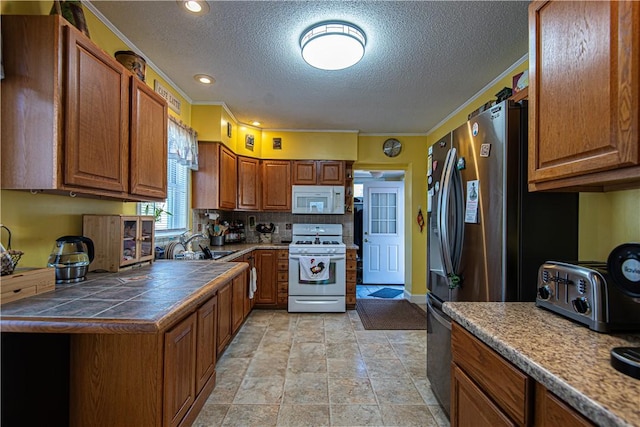 kitchen with white appliances, a sink, tile counters, brown cabinetry, and crown molding