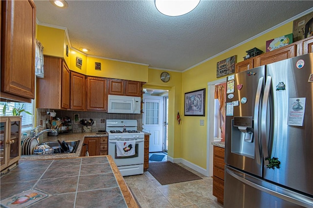 kitchen with tile countertops, white appliances, a sink, ornamental molding, and brown cabinets