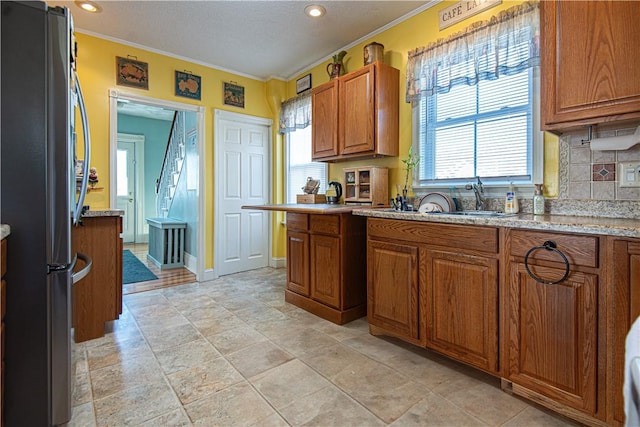 kitchen with brown cabinetry, freestanding refrigerator, ornamental molding, and backsplash