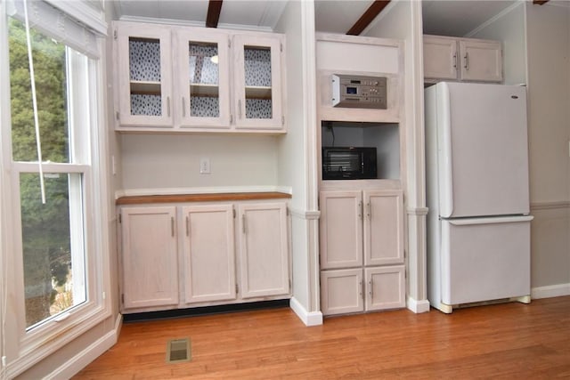 kitchen featuring light countertops, light wood-style flooring, glass insert cabinets, and freestanding refrigerator