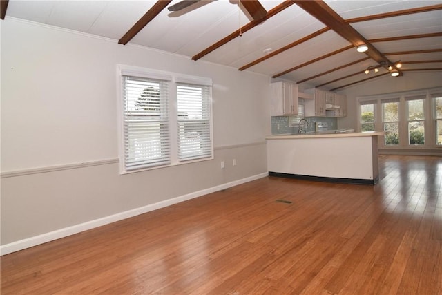 unfurnished living room with lofted ceiling with beams, plenty of natural light, wood finished floors, and baseboards