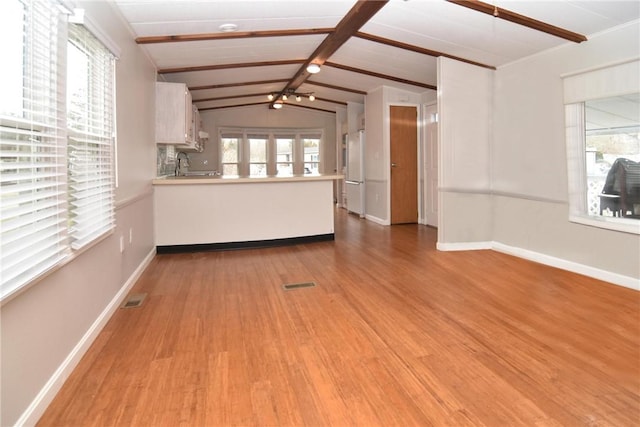 unfurnished living room featuring a healthy amount of sunlight, vaulted ceiling with beams, visible vents, and light wood finished floors