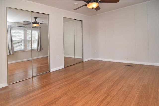 unfurnished bedroom with light wood finished floors, visible vents, multiple closets, and ornamental molding