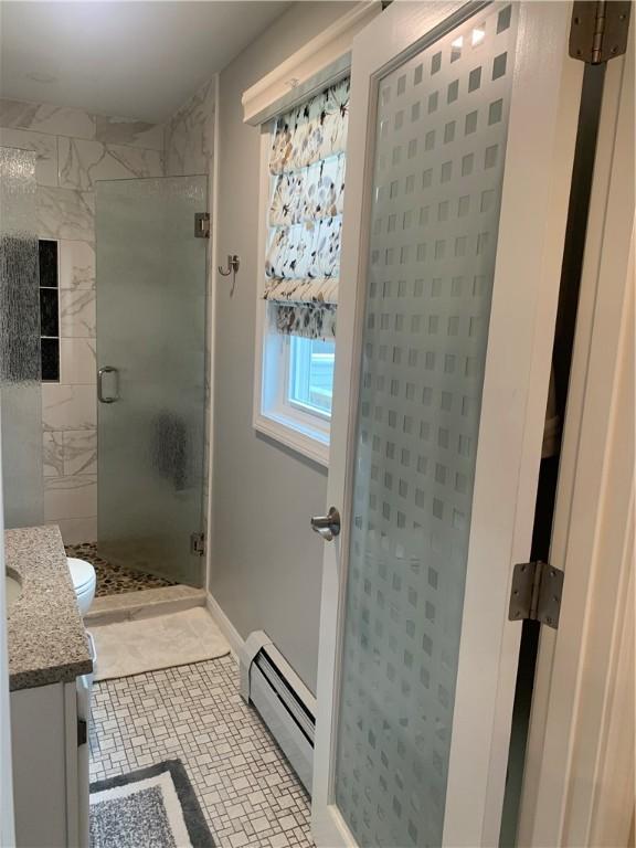 full bathroom with toilet, a baseboard heating unit, vanity, baseboards, and a shower stall