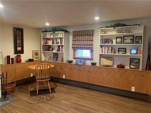 living area with a paneled ceiling, a baseboard radiator, and wood finished floors