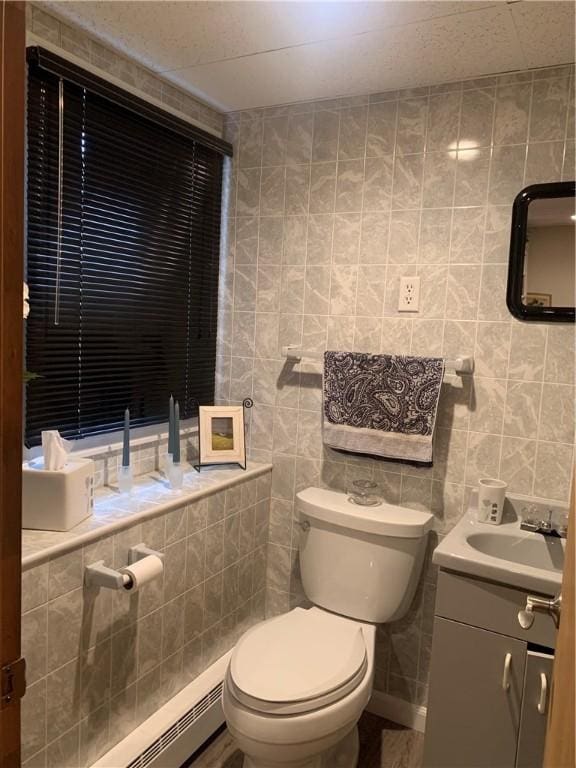 bathroom featuring toilet, a baseboard heating unit, and tile walls