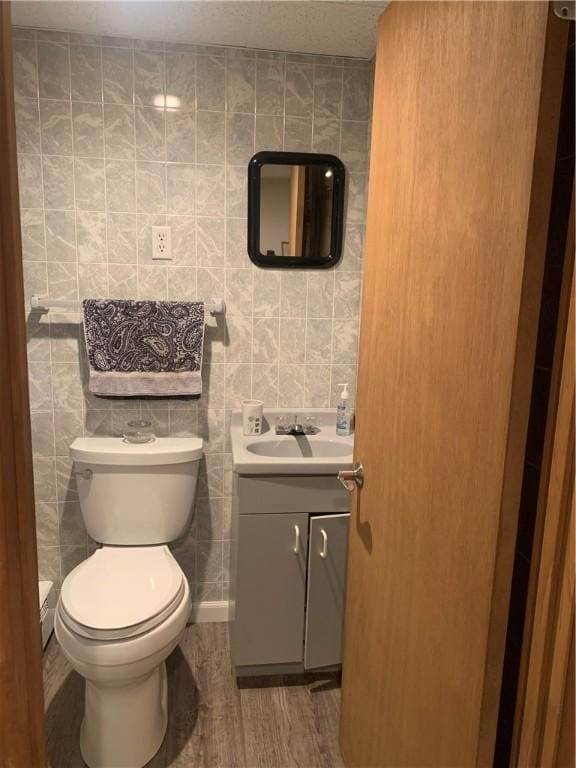 bathroom featuring toilet, wood finished floors, vanity, and tile walls