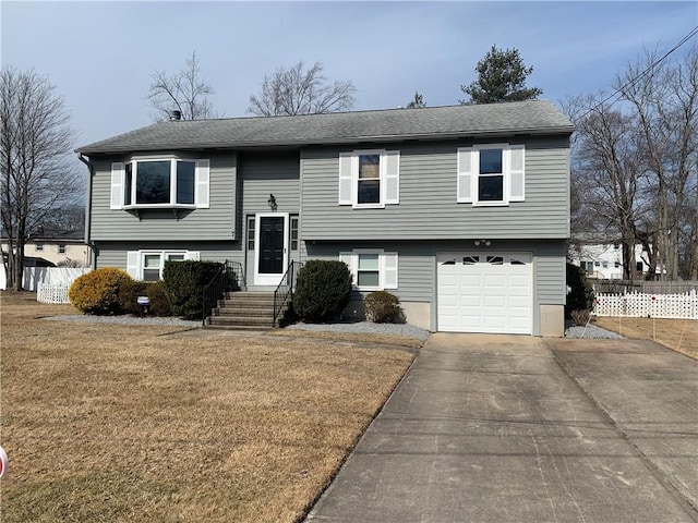 raised ranch featuring entry steps, concrete driveway, an attached garage, fence, and a front lawn