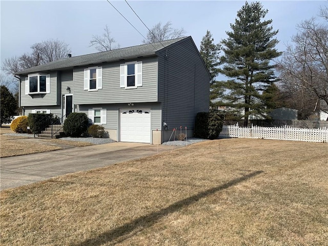 bi-level home with an attached garage, driveway, a front yard, and fence