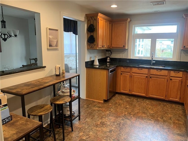 kitchen featuring recessed lighting, a sink, stainless steel dishwasher, brown cabinetry, and dark countertops