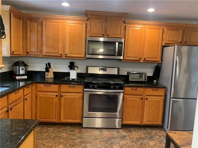 kitchen featuring stainless steel appliances, recessed lighting, brown cabinets, and dark stone countertops