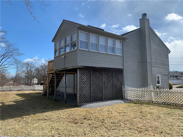 rear view of house with stairway, a chimney, fence, and a lawn