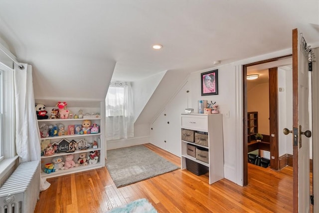 game room featuring lofted ceiling, light wood-style flooring, and radiator