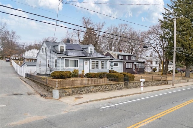 view of front of home featuring a chimney, a fenced front yard, and roof mounted solar panels