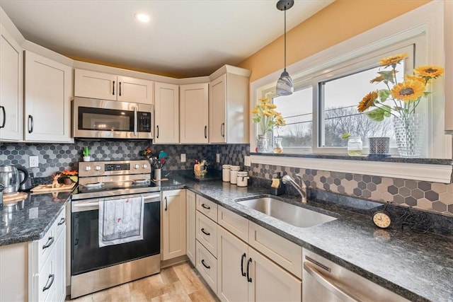 kitchen with pendant lighting, light wood finished floors, stainless steel appliances, tasteful backsplash, and a sink