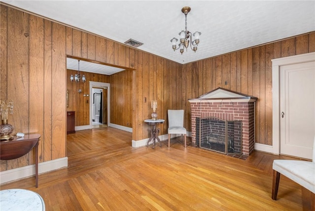 living area with a brick fireplace, visible vents, a chandelier, and wood finished floors